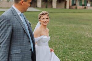 A handsome groom and an elegant bride in a lush white dress are walking in a summer park. Happy bride and groom getting ready for their best day. photo