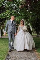 A handsome groom and an elegant bride in a lush white dress are walking in a summer park. Happy bride and groom getting ready for their best day. photo