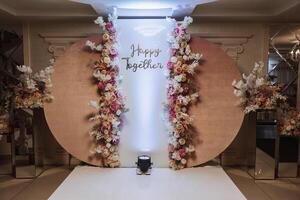 The photo zone at a wedding or birthday celebration is decorated with flowers and illuminated by artificial light