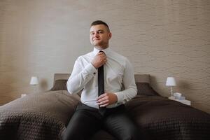 man in shirt dressing up and adjusting tie on neck at home. Wedding day concept,fashion, business, male style. photo