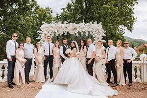 The bride and groom and their friends pose near the arch. Long train of the dress. Stylish wedding. Summer wedding in nature photo