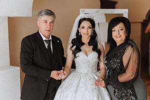 contento padres sostener el manos de el novia quien es consiguiendo casado y apoyo su, vistiendo un Boda vestir y un largo velo. foto