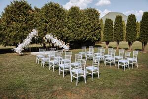 Decorative modern wedding arch made of white flowers in nature. Many white chairs for the wedding ceremony. Everything is ready for the celebration. photo