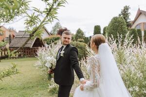 A handsome groom and an elegant bride in a lush white dress are walking in a summer park. Happy bride and groom getting ready for their best day. photo