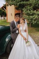 A handsome groom embraces his bride in a lush white dress and smiles in a beautiful outdoor setting. Under the open sky. High quality photo. A newlywed couple poses together on a sunny summer day. photo