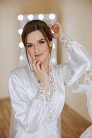 A beautiful bride with a long veil in her room, wearing a robe. Wedding dress on a mannequin. The bride in the morning before the wedding ceremony. photo