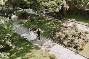 A handsome groom and an elegant bride in a lush white dress are walking in a summer park. Happy bride and groom getting ready for their best day. photo