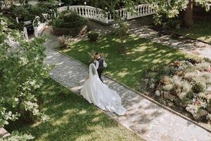 A handsome groom and an elegant bride in a lush white dress are walking in a summer park. Happy bride and groom getting ready for their best day. photo