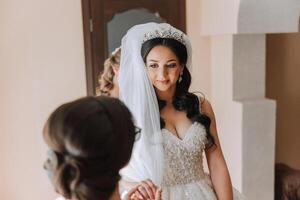 Boda Mañana. damas de honor ayuda poner en el blanco Boda vestido. un joven mujer es preparando a reunirse su novio y teniendo divertido con su amigos foto