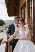 A handsome groom embraces his bride in a lush white dress and smiles in a beautiful outdoor setting. Under the open sky. High quality photo. A newlywed couple poses together on a sunny summer day. photo