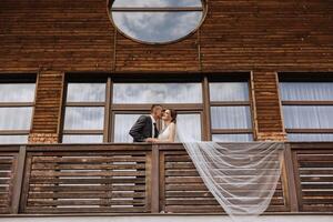 a newly married couple. the wind lifts a long white veil in summer. The bride and groom are hugging, a long veil is blowing in the wind. The newlyweds kiss on the balcony of the restaurant photo