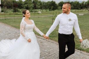 A handsome groom and an elegant bride in a lush white dress are walking in a summer park. Happy bride and groom getting ready for their best day. photo