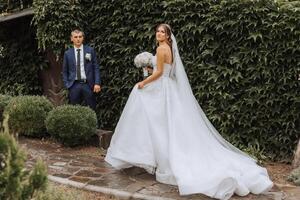 The bride is dressed in an elegant lush white wedding dress with a long veil and is ready for her groom. The first meeting of the bride and groom photo