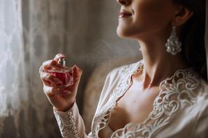 A beautiful young bride girl holds an elegant bottle of perfume in her hand and is ready to spray herself. Morning of the bride before the wedding ceremony. photo