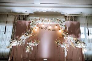 The photo zone at a wedding or birthday celebration is decorated with flowers and illuminated by artificial light