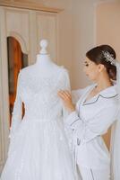 A beautiful bride is sitting in a dressing gown in the morning before the wedding ceremony in a hotel with a modern interior. Incredible hairstyle of the bride. Natural and modern makeup. photo