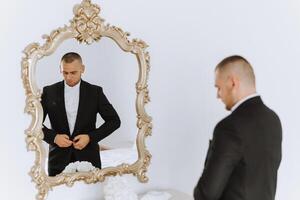 un hombre sujeta el botones en su chaqueta en frente de un espejo. novio en un traje. arriba cerca el hombre sujeta su chaleco. Perfecto abajo a el último detalle. moderno empresario. foto