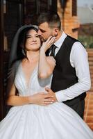 A handsome groom embraces his bride in a lush white dress and smiles in a beautiful outdoor setting. Under the open sky. High quality photo. A newlywed couple poses together on a sunny summer day. photo