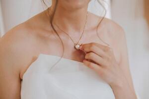 Morning preparation of the bride. Necklace on the neck. Pendant on a gold chain on a woman's breast. Beautiful decollete. Closeup. photo