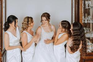 Wedding morning. Bridesmaids help put on the white wedding dress. A young woman is preparing to meet her groom and having fun with her friends photo