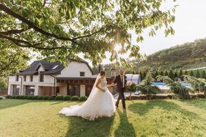 A handsome groom and an elegant bride in a lush white dress are walking in a summer park. Happy bride and groom getting ready for their best day. photo