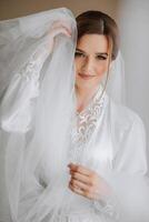 Beautiful bride in a dressing gown in the morning before the wedding ceremony. Incredible hairstyle of the bride. Natural and modern makeup. Portrait of a young bride in a dressing gown. photo