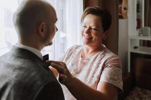 madre ayuda su adulto hijo preparar para el Boda ceremonia. un emocional y conmovedor momento a un boda. un madre abrazos su hijo foto