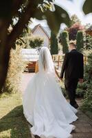 A handsome groom and an elegant bride in a lush white dress are walking in a summer park. Happy bride and groom getting ready for their best day. photo