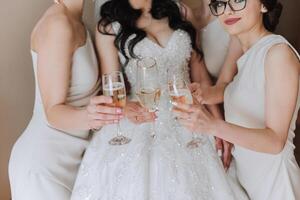 Photo bride with her friends drinking champagne from glasses. Cropped shot of a beautiful young bride and her bridesmaids having champagne before the wedding.