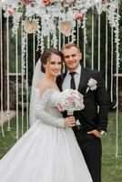 A handsome groom embraces his bride in a lush white dress and smiles in a beautiful outdoor setting. Under the open sky. High quality photo. A newlywed couple poses together on a sunny summer day. photo