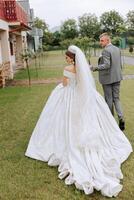 A handsome groom and an elegant bride in a lush white dress are walking in a summer park. Happy bride and groom getting ready for their best day. photo