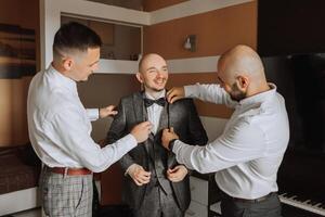 elegante novio riendo y teniendo divertido con padrinos de boda mientras consiguiendo Listo en el Mañana para Boda ceremonia. lujo hombre foto