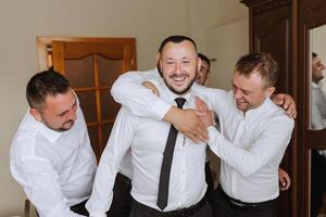 elegante novio riendo y teniendo divertido con padrinos de boda mientras consiguiendo Listo en el Mañana para Boda ceremonia. lujo hombre foto