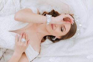 A beautiful bride in a white dress is lying. A girl in a white dress is resting. Beautiful hair and makeup. The model poses for the photographer. photo