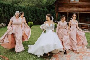 A brunette bride and her bridesmaids in identical pink dresses are walking against the background of nature. Girls in identical dresses are making out at a wedding. Wedding in nature. photo