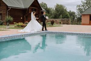 A handsome groom and an elegant bride in a lush white dress are walking in a summer park. Happy bride and groom getting ready for their best day. photo