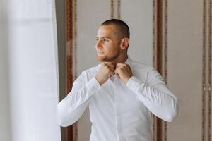 negocio camisa. un hombre en un blanco camisa sujeta el botones. joven político, masculino estilo, empresario abotonarse camisa, masculino manos de cerca, americano, europeo empresario foto