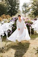 A beautiful brunette bride in an elegant robe is walking in a park with green grass and pink hydrangea flowers. Morning, meetings, wedding portrait of a cute girl. Photography and concept. Summer. photo