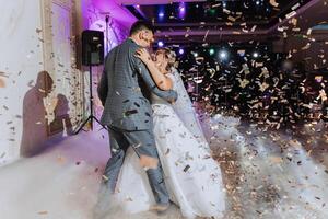 Wedding dance of the bride and groom. The first dance of the bride and groom in an elegant wedding hall with the use of heavy smoke and pyrotechnic lights, confetti. photo