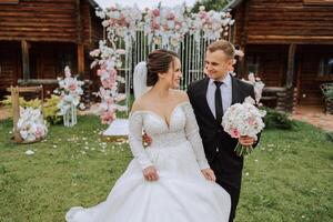 A handsome groom and an elegant bride in a lush white dress are walking in a summer park. Happy bride and groom getting ready for their best day. photo