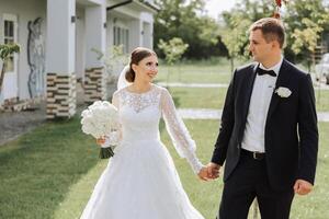 A handsome groom and an elegant bride in a lush white dress are walking in a summer park. Happy bride and groom getting ready for their best day. photo