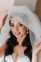 retrato de el novia en el hotel habitación. un hermosa joven niña es vestido en un blanco Boda vestido. moderno Boda peinado. natural constituir. foto