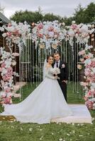 un hermoso novio abraza su novia en un lozano blanco vestir y sonrisas en un hermosa al aire libre ajuste. debajo el abierto cielo. alto calidad foto. un recién casado Pareja poses juntos en un soleado verano día. foto