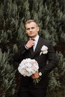 retrato de el novio en naturaleza en el verano. elegante alto novio en un elegante negro negocio traje. empresario en naturaleza. retrato de un exitoso hombre. Boda retrato de el novio. foto