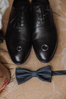 On the floor are men's dark leather shoes and a black belt, a man's suit on a mannequin, a wedding bouquet of flowers, wedding rings, men's perfume. Photo, top view. photo