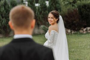 el novia es vestido en un elegante lozano blanco Boda vestir con un largo velo y es Listo para su novio. el primero reunión de el novia y novio foto