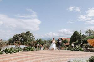 A handsome groom and an elegant bride in a lush white dress are walking in a summer park. Happy bride and groom getting ready for their best day. photo