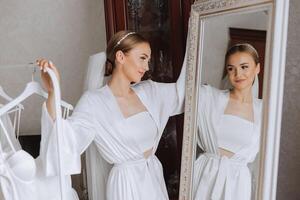 A beautiful bride with a long veil in her room, wearing a robe. Wedding dress on a mannequin. The bride in the morning before the wedding ceremony. photo