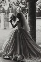 Photo from the back. A beautiful young woman in a white wedding dress is smiling on a warm wedding summer day