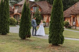 A handsome groom and an elegant bride in a lush white dress are walking in a summer park. Happy bride and groom getting ready for their best day. photo